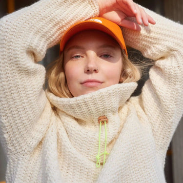 Model wearing cozy crocheted sweater from Hooks Out collection with bright orange cap.