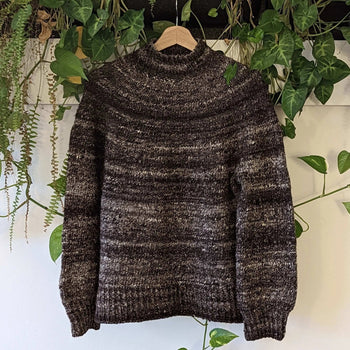 Hand-knitted jumper hanging with green plants, part of the Knitted Jumper Workshop offerings.