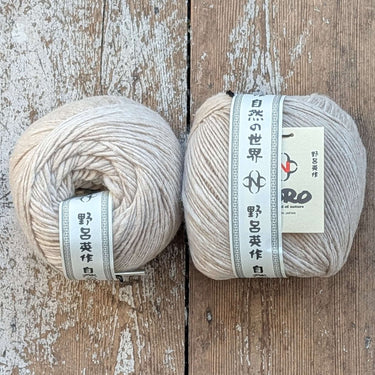 Two barrels of Noro Haunui natural merino wool yarn on a wooden surface.