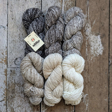 Four skeins of Noro Haunui Silk yarn in natural shades of gray and brown, made from raw mulberry silk and Haunui merino wool.