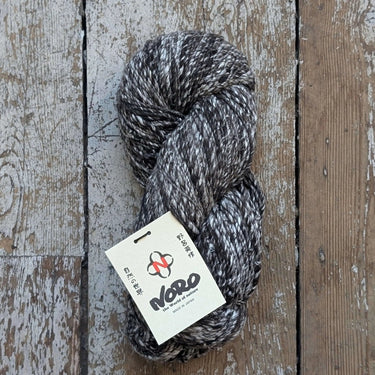 Noro Haunui Silk yarn skein made from mulberry silk and Haunui merino wool, undyed, displayed on rustic wooden background.