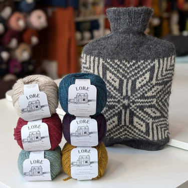 Pochie Hot Water Bottle with knitted cover and yarns, featuring Lore yarns for Knitting Kit by Kate Davies, perfect for cozy warmth.
