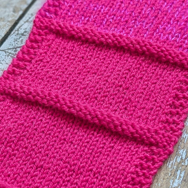 Pink knitted swatch in Gepard Pure Lana yarn on a wooden surface
