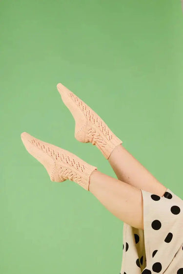 Cream lace knit socks modeled against a green background - Knitting Book inspiration