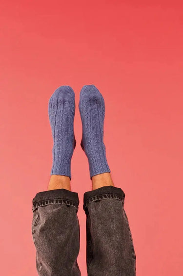 Blue knitted socks on feet against a pink background, showcasing a pattern from Ready Steady Sock | Knitting Book.
