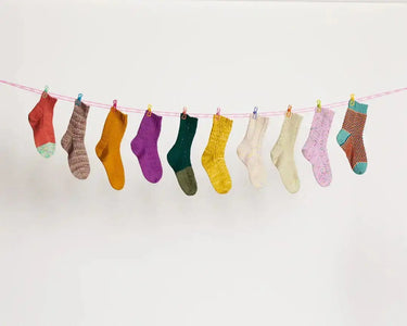 Colorful hand-knitted socks hanging, showcasing designs from Ready Set Socks by Pom Pom; essential for any Knitting Book enthusiast.