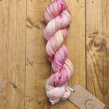A skein of hand-dyed A&P Classic Sock 4ply yarn in pink hues, perfect for knitting durable and soft socks, hats, and accessories.