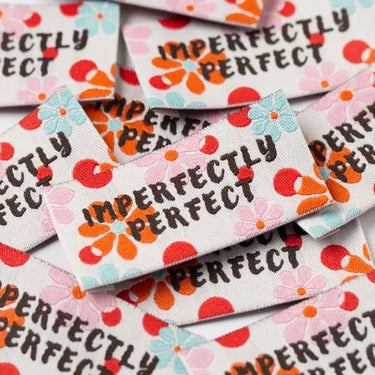 Embroidered patches with 'IMPERFECTLY PERFECT' text and floral designs on a pile.