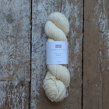 A skein of cream-colored yarn with a white paper label, placed vertically on a rustic, weathered wooden plank surface.