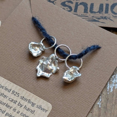 Handcrafted Silver Stitch Markers made from recycled 925 silver, featuring unique water-cast organic shapes, displayed on a brown card.