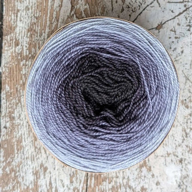 Top view of a ball of Snek gradient hand-dyed merino wool yarn with a color shift from black to grey.