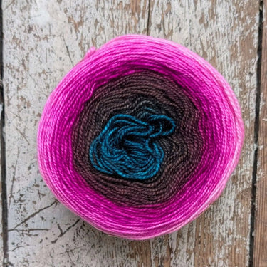 Gradient hand-dyed merino wool, Snek by Bilum, in pink, brown, and blue tones on wooden surface.