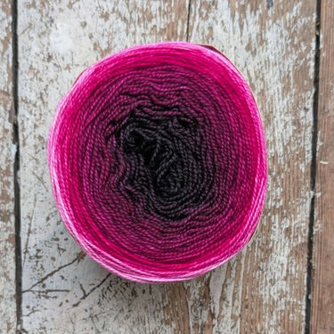 Snek gradient hand-dyed soft merino wool yarn in pink and black on wooden surface
