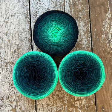 Three skeins of green and black yarn on a wooden surface