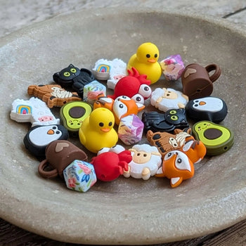 Colorful assortment of Stitch Stoppers by Fox & Pine Stitches in a bowl, featuring rubber duck and animal designs for knitting.