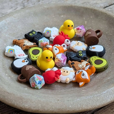 Colorful assortment of Stitch Stoppers by Fox & Pine Stitches in a bowl, featuring rubber duck and animal designs for knitting.