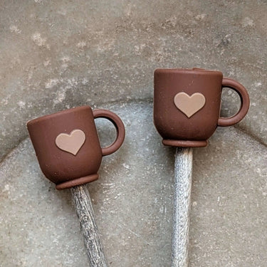 Brown mug-shaped Stitch Stoppers with heart design by Fox & Pine Stitches on knitting needles.