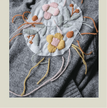 Floral knitwear repair on gray fabric, illustrating techniques from The Art of Knitwear Repair by Minttu Wikberg.