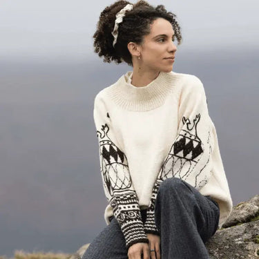 Woman wearing a wool sweater inspired by A Knitter's Guide sitting outdoors, showcasing intricate sheep patterns.