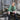 Woman in a green sweater and black rain boots sitting on a wooden platform in front of a rustic wooden building. Tukubook knitting book