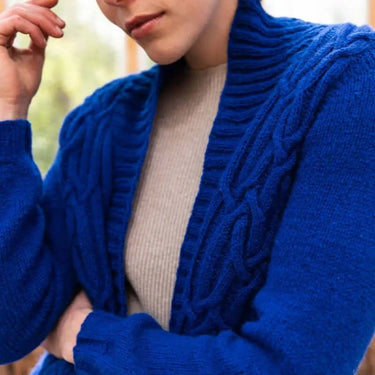 Person wearing a blue knitted cardigan with a blurred background. Tukubook knitting book