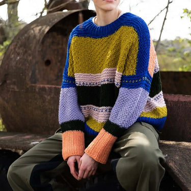 Person wearing a colorful striped sweater sitting outdoors. Tukubook knitting book