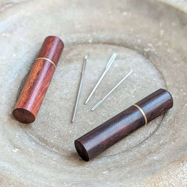 Darning Needles with wooden cases in light and dark brown displayed on a textured surface, showcasing quality craftsmanship by Fox & Pine Stitches.