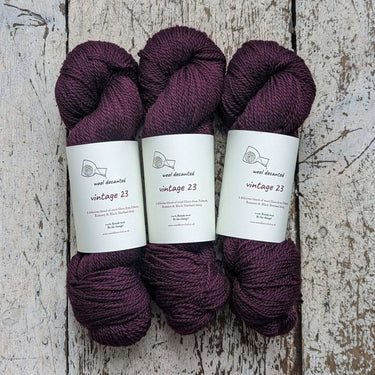 Three skeins of Wool Decanted Vintage 23, soft British 4ply Yarn in deep burgundy, displayed on wooden table