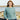 Woman wearing a blue sweater from Aran by Marie Wallin collection, featuring intricate cable knitting design, standing near the sea.