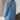 Woman wearing a blue knitted sweater with floral patterns on the back, sitting against a neutral wall.