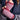 Close-up of pink and red knitted fingerless gloves held by a person wearing a blue sweater.