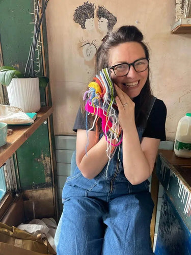Knit With Me shop Owner Carol holding yarn swatches to her face