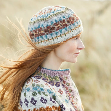 Woman wearing hand-knitted hat and sweater using British Breeds Aran Gift Box yarn, showcasing colorful patterns in an outdoor setting.