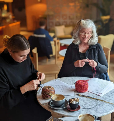 Two women sitting at a table in a Knitting lesson both knitting