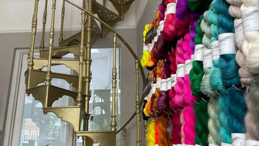 Colorful yarn skeins hanging on a wall next to a gold spiral staircase