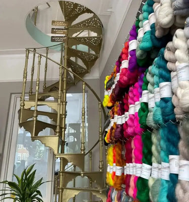 Gold spiral staircase next to a wall of colorful yarn.
