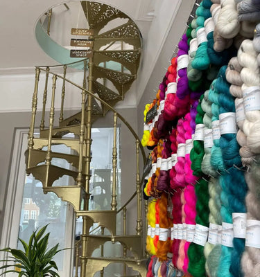 Gold spiral staircase next to a wall of colourful yarn inside Knit With Me, Richmond, London, yarn shop