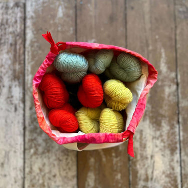 Top view of a vibrant ice dyed Craft Project Bag filled with colorful yarn skeins on a wooden floor.