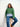 Woman wearing green sweater from "52 Weeks of Sweaters" knitting book collection, seated on stool.