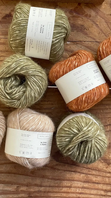 Skeins of Le Coton & Alpaca yarn in various colors on a wooden surface, ideal for spring and autumn knitting projects.