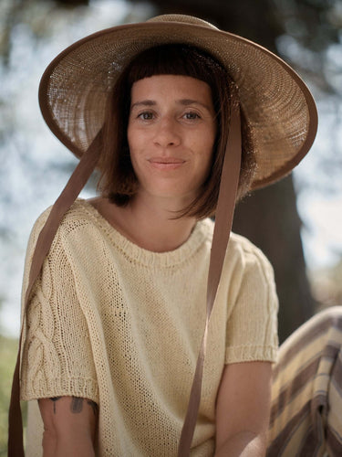 Woman wearing a straw hat and a knitted top outdoors, featured in Laine Magazine Spring Issue 28.
