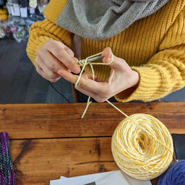 Person learning knitting in Beginner Knitting Class with yellow yarn.