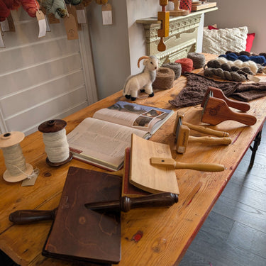 Yarn spinning class setup with tools, a toy sheep, and skeins of wool on a wooden table.