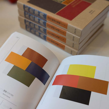 Open page of 'The Japanese Dictionary of Colour Combinations' by Sanzo Wada showcasing color palettes with books stacked in the background.
