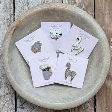 Twill + Print Enamel Pins featuring Little White Sheep, Glitter Sheep, Alpaca on display in a bowl, perfect for accessories.