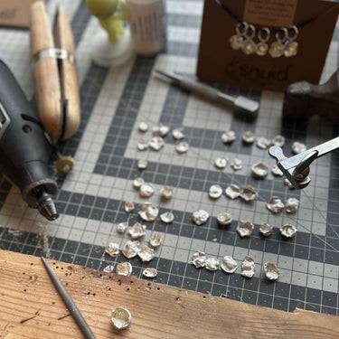 Handcrafted Silver Stitch Markers in workshop with tools and materials displayed on a crafting table.