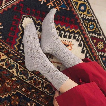 Hand-knit socks from Amirisu Sock Knitting Club showcasing intricate patterns on a colorful rug.