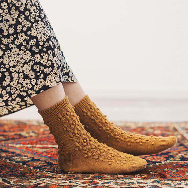 Amirisu Sock Knitting Club textured socks on a colorful rug, showcasing intricate knitting designs for enthusiasts.