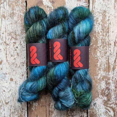 Three skeins of A&P Lace Silk Mohair yarn in shades of blue and green, hand dyed for unique softness and texture.