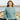 Woman wearing a blue sweater from Aran by Marie Wallin collection, featuring intricate cable knitting design, standing near the sea.